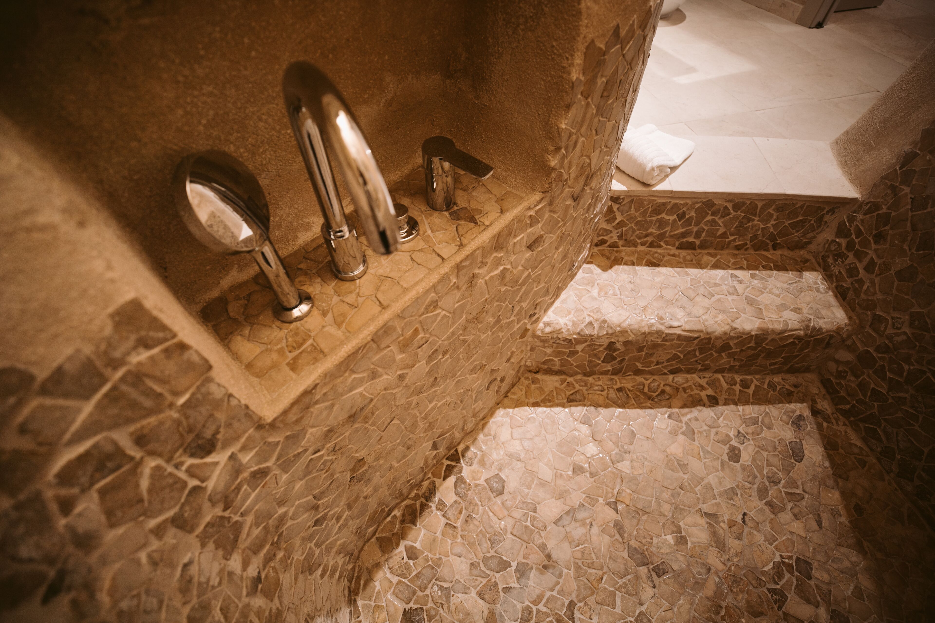 A bathroom with a mosaic floor and a bathtub with a faucet and a mirror.