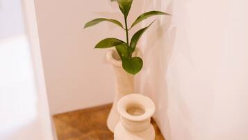 A white vase with a plant on a wooden surface against a white wall.