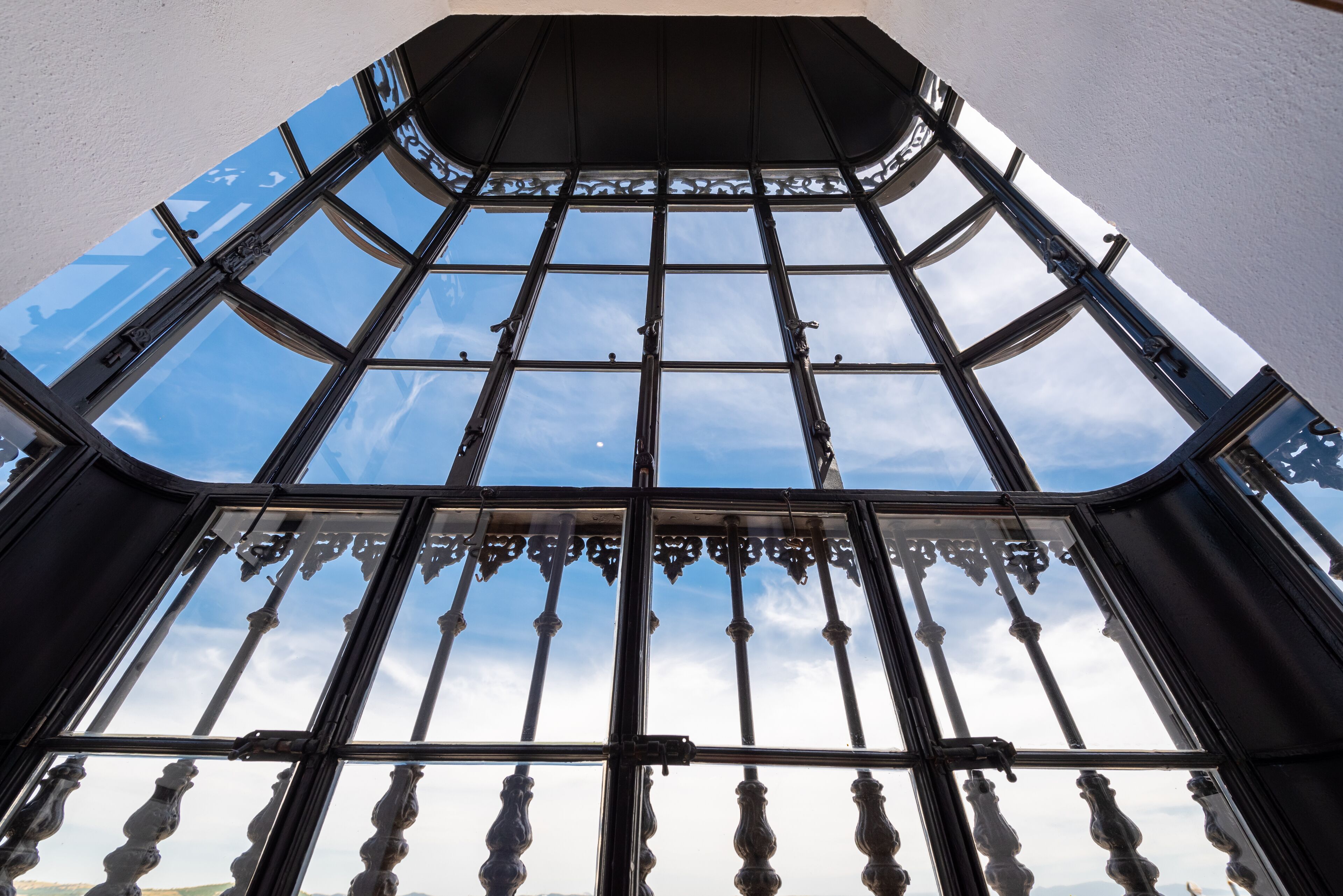 Un plafond haut, surmonté d’une grande verrière ornée de balustrades en métal ouvragé, offrant une vue dégagée sur le ciel.