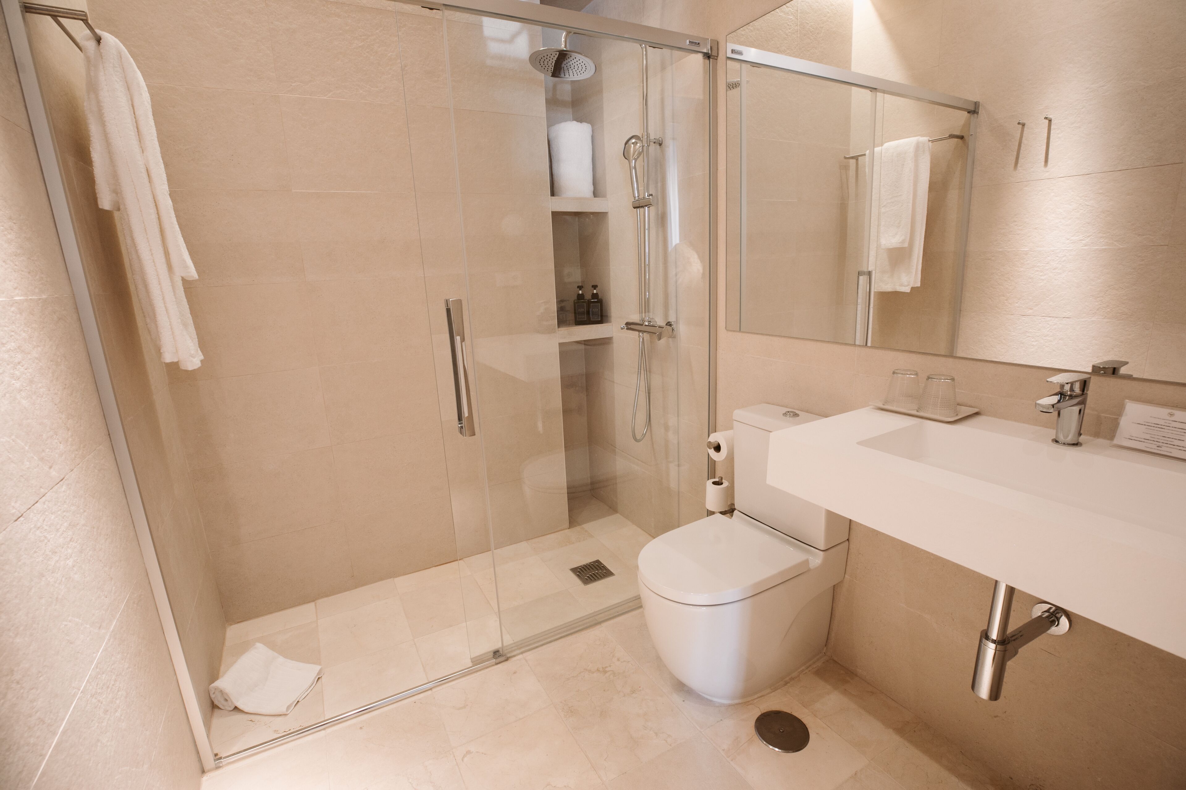 A modern bathroom with a glass-enclosed shower, a white toilet, and a sink with a mirror above it.