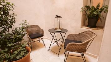 A small, cozy seating area with wicker chairs and a table, surrounded by potted plants.