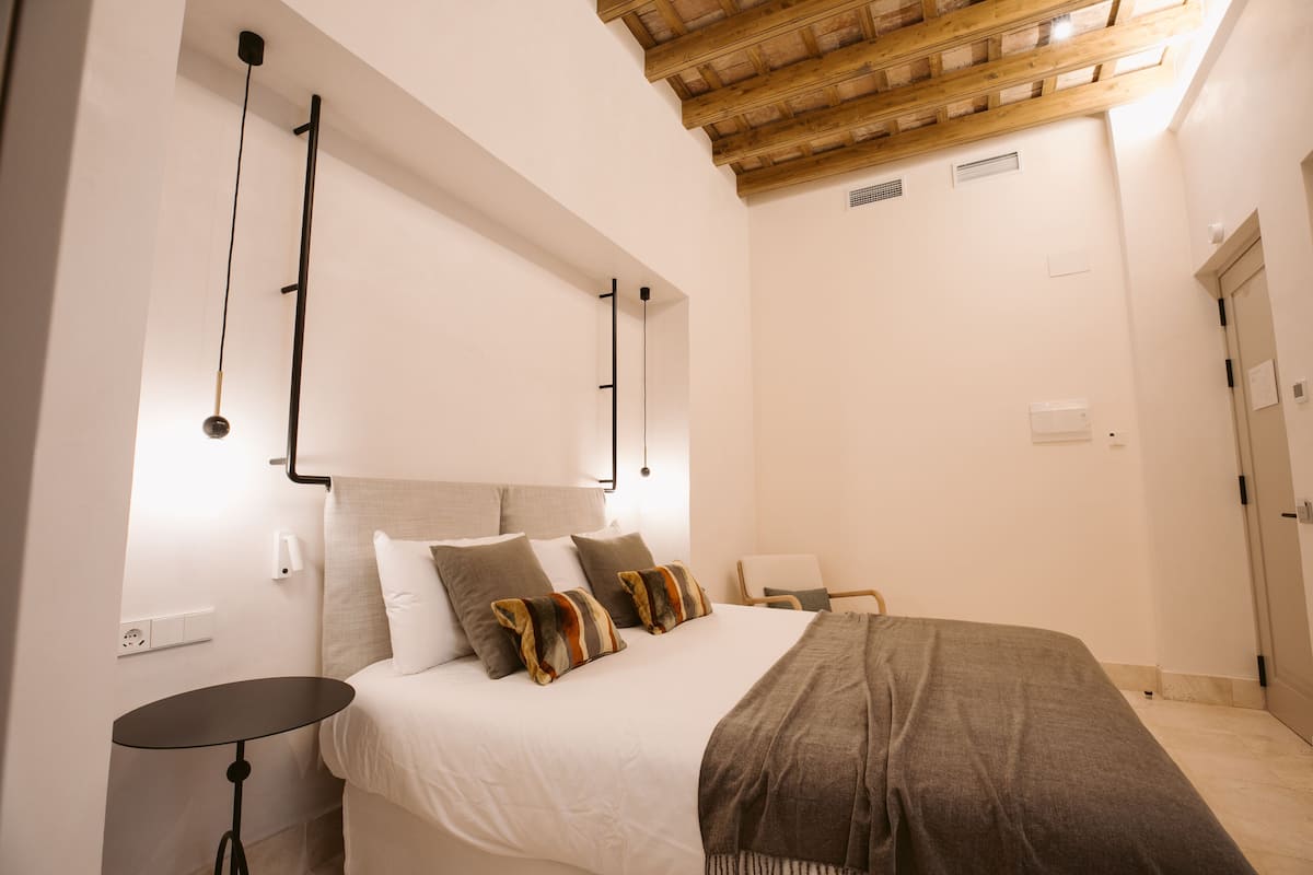 Un dormitorio con cama, mesitas de noche, techo de madera y una puerta.