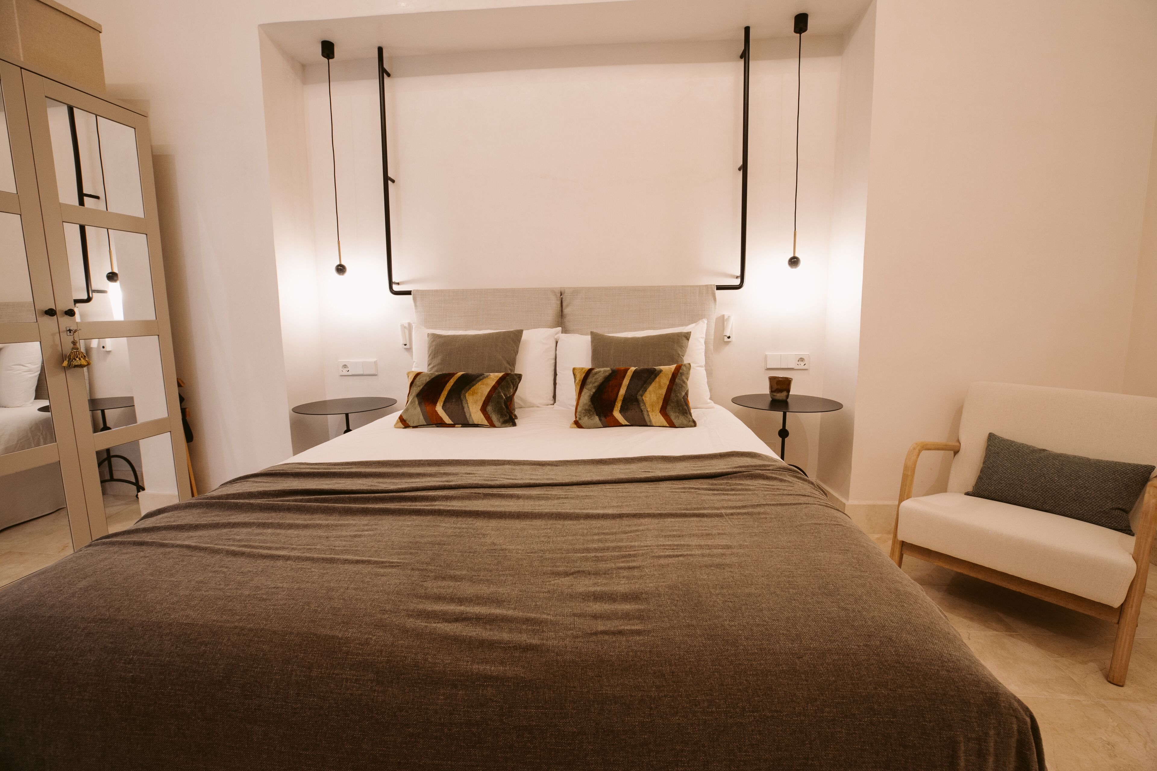 A modern hotel room with a large bed, two bedside tables, a chair, and a wardrobe.