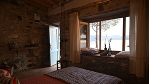 Una habitación rústica con una cama, una mesita, un ventanal con vistas a un lago y una puerta que da al exterior.