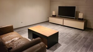 Uma sala de estar moderna com um sofá de couro, uma mesa de centro de madeira, uma televisão de tela plana em um suporte de madeira e um sistema de entretenimento embutido com alto-falantes.
