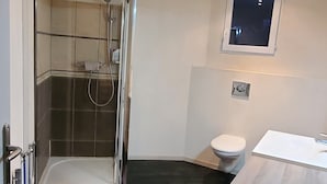 Uma casa de banho moderna com cabine de duche em vidro, sanita e lavatório.
