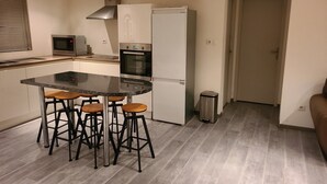 Uma cozinha moderna com uma ilha central, banquetas, micro-ondas, forno e lixeira.
