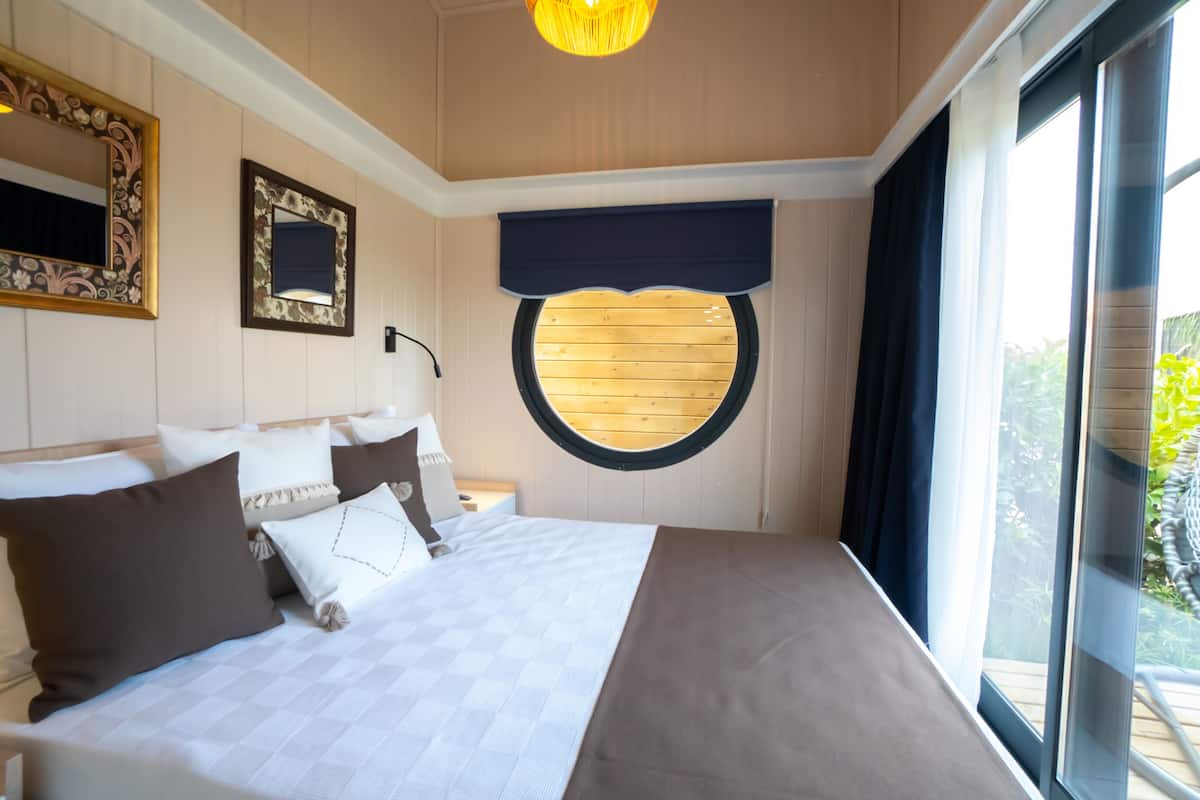 Quarto com uma cama grande, uma janela redonda e vista para o exterior.