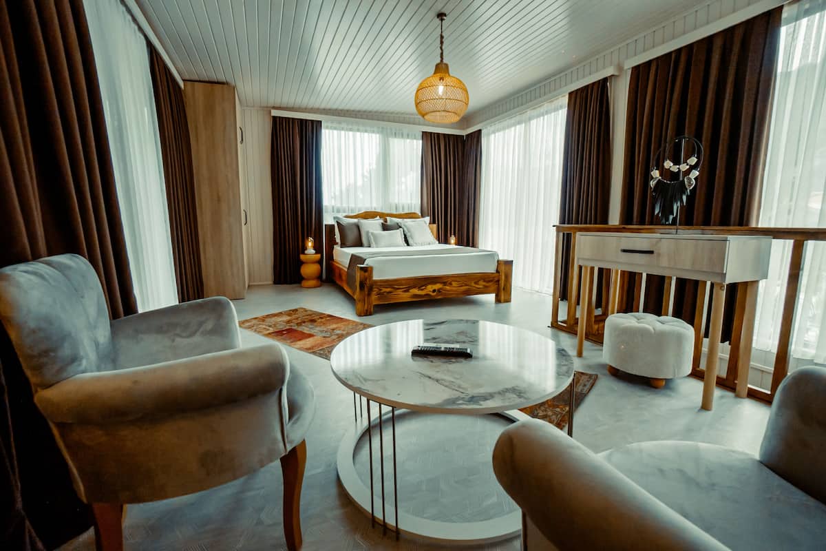 Quarto de hotel moderno com cama, dois poltronas, uma mesa de centro redonda e uma escrivaninha com cadeira.