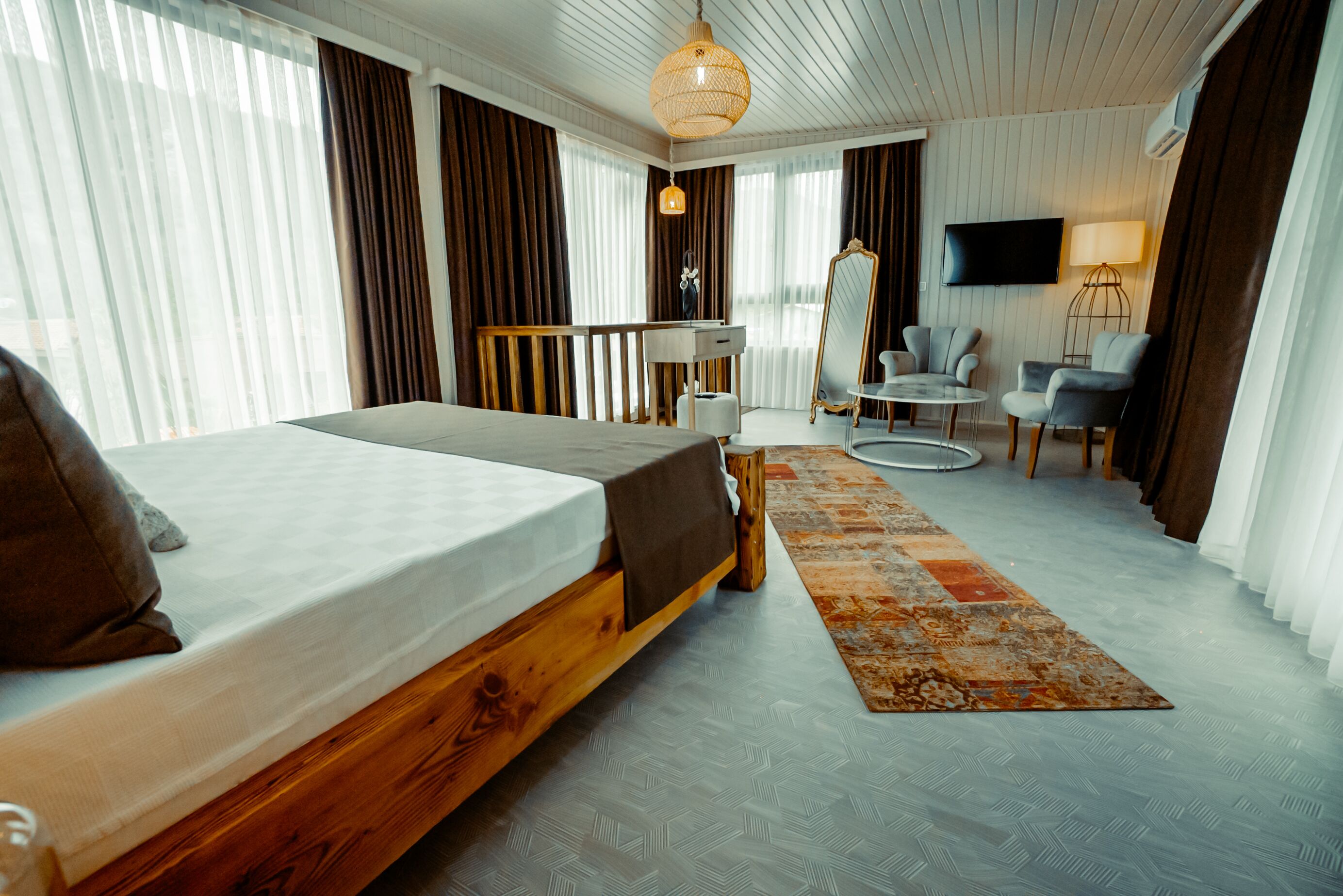 A hotel room with a wooden bed, a desk, a chair, a TV, and a large window with curtains.