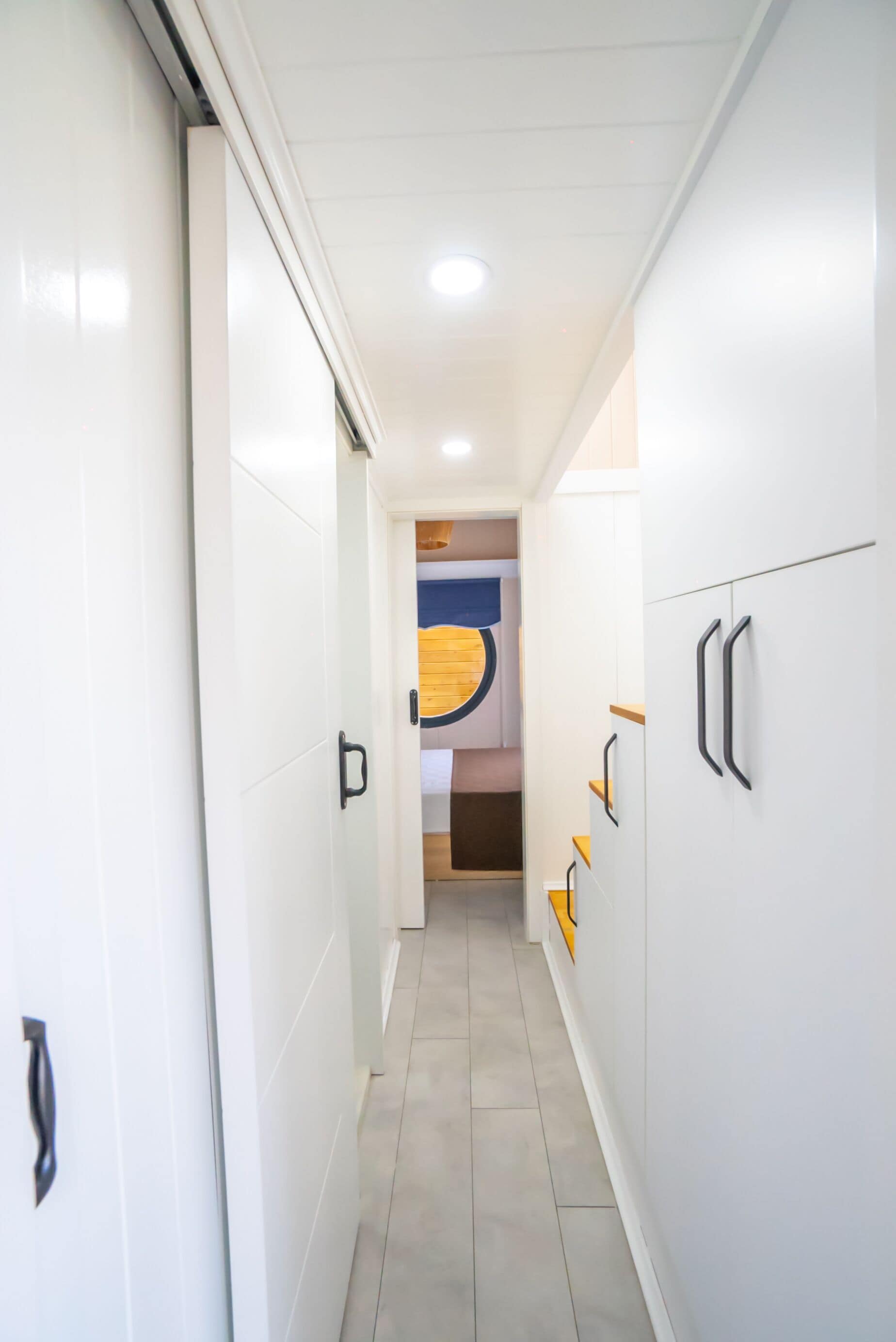 A hallway with white walls, a tiled floor, and a door on the left.