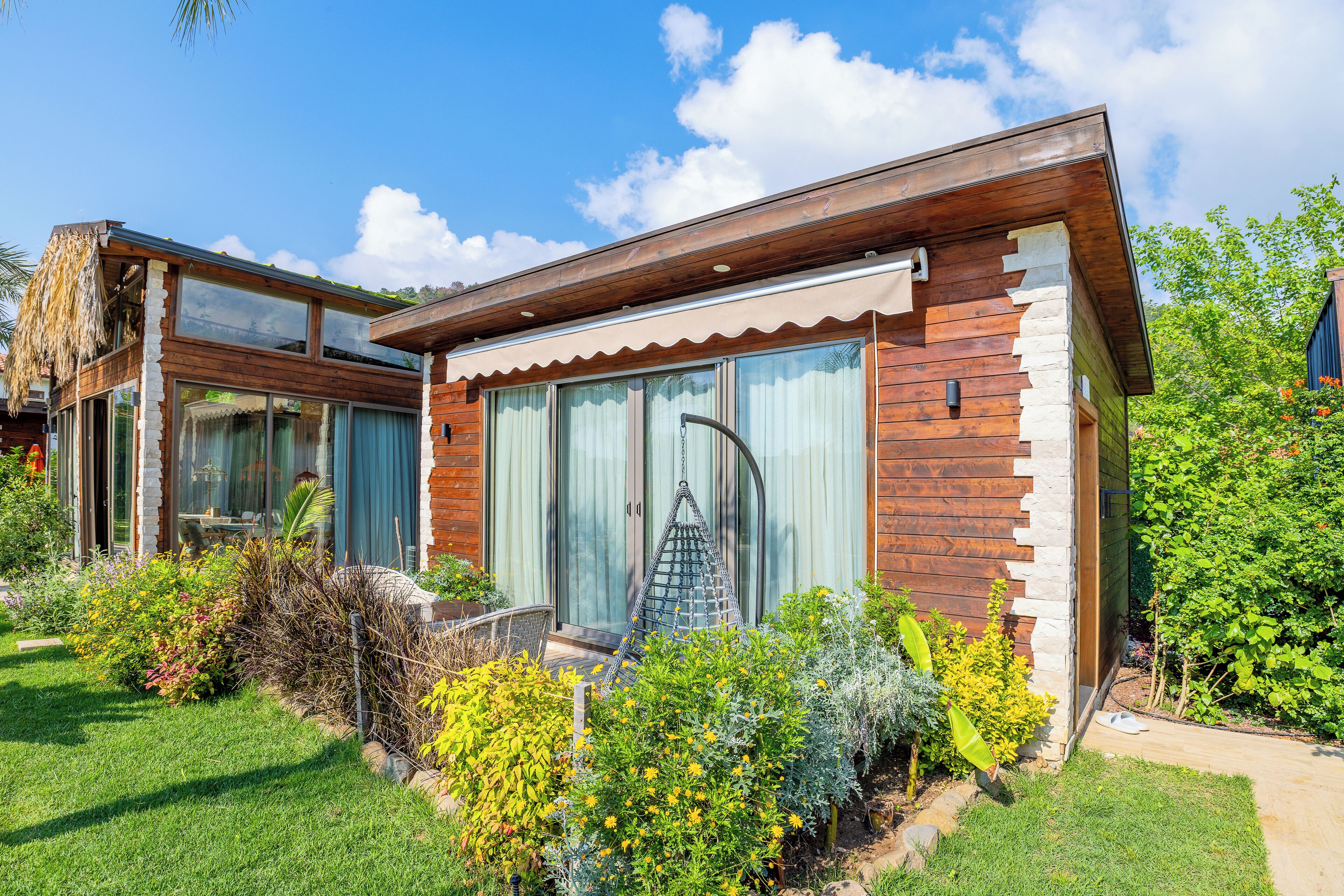 A modern house with a large glass door, a wooden exterior, and a garden with various plants.
