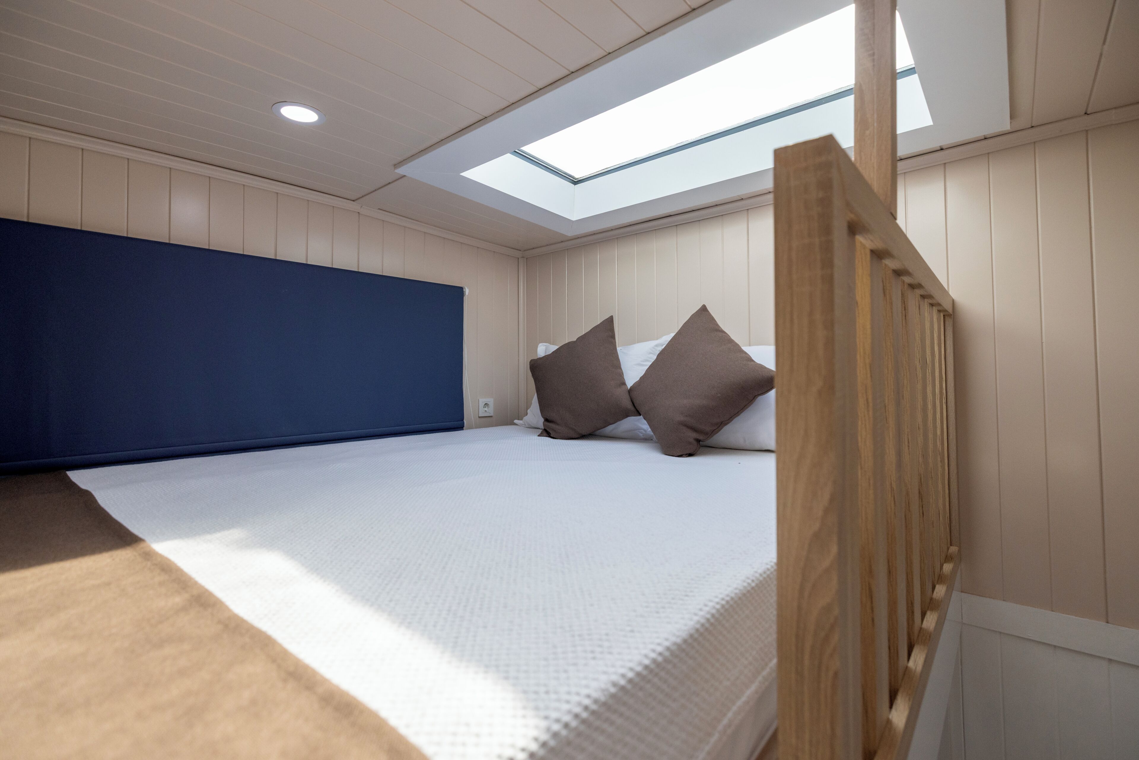 A bedroom with a skylight, a bed with pillows, and a wooden headboard.