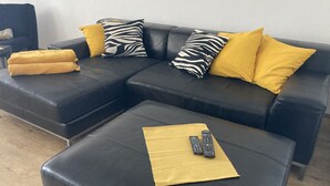 A sectional sofa with yellow and zebra-patterned pillows, a matching ottoman, and two remote controls on a yellow cloth.