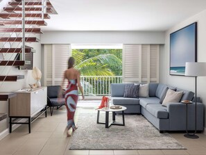 Una sala de estar moderna con una escalera, un sofá, una mesa de centro y vistas al exterior con vegetación.