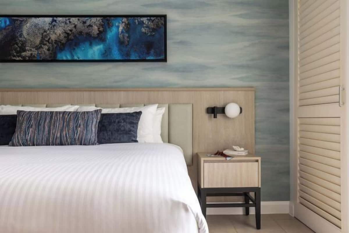 Habitación de hotel ordenada con una cama grande, una mesita de noche con lámpara y una obra de arte colgada en la pared.