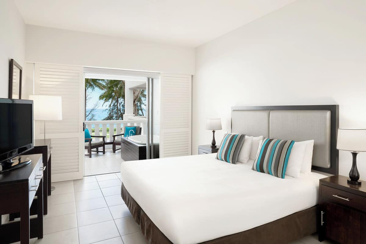 Habitación de hotel con cama, televisión, escritorio y silla, y vista al océano.