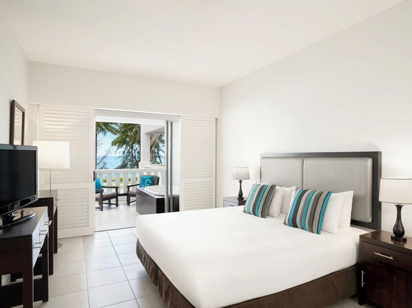 A hotel room with a bed, a TV, a desk with a chair, and a view of the ocean. - Peppers Beach Club & Spa Palm Cove (Cairns)
