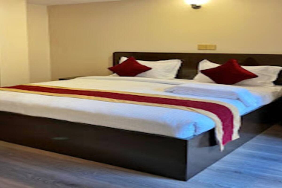 Ein ordentlich bezogenes Bett mit weißer Bettwäsche und roten Akzenten, ein dunkles Kopfbrett und eine helle Wand.