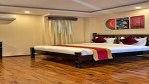 Hotelkamer met een houten vloer, een groot bed met wit beddengoed en rode kussens, een raam met gordijnen, en een wand met kleurrijke kunstwerken.