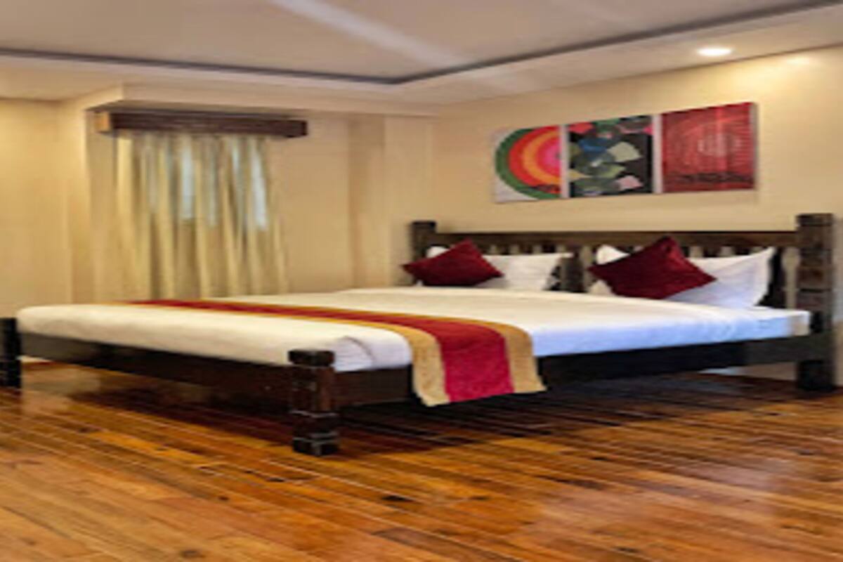 Ein Hotelzimmer mit Holzboden, einem großen Bett mit weißer Bettwäsche und roten Kissen, einem Fenster mit Vorhängen und einer Wand mit farbenfroher Kunst.