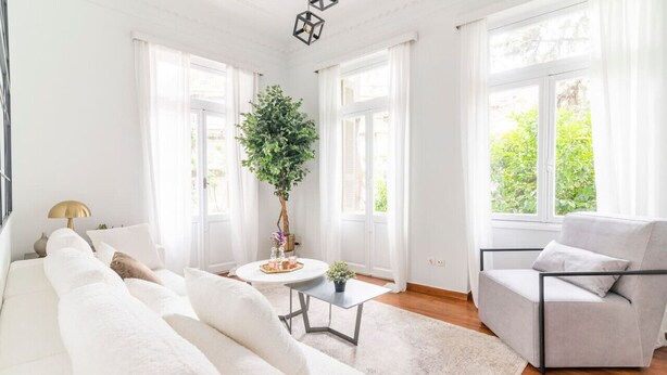 Un salon lumineux avec un canapé blanc, un fauteuil gris, une table basse ronde et une plante en pot.