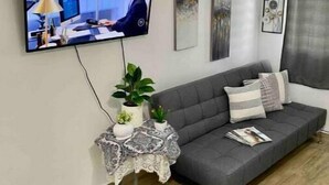 A modern living room with a grey sofa, a small side table with decorative items, a television mounted on the wall, and a ceiling light fixture. - Unidad 1 - Casa Cuatro Palmas 🌴 (rincon)