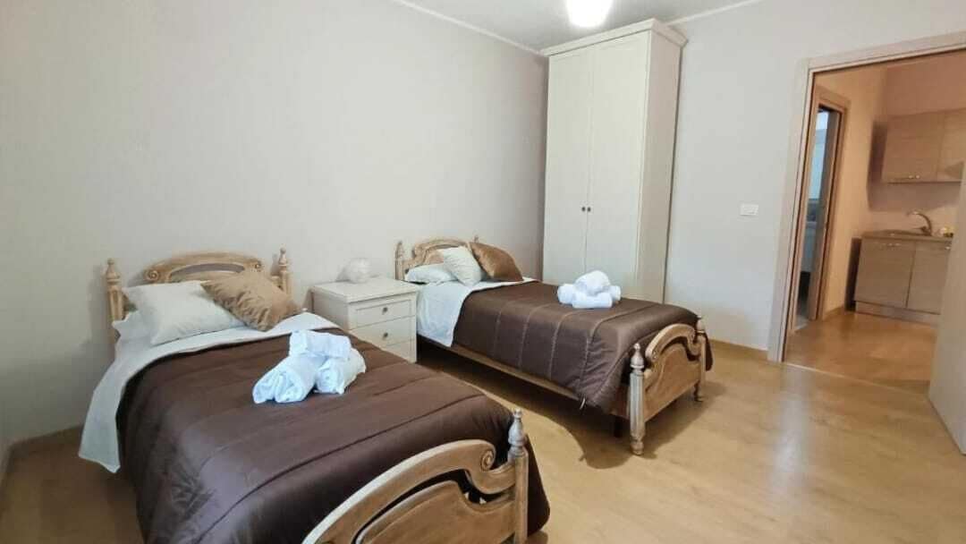 Een slaapkamer met twee houten bedden, een nachtkastje, een kledingkast en een zichtbare badkamer door een open deur.
