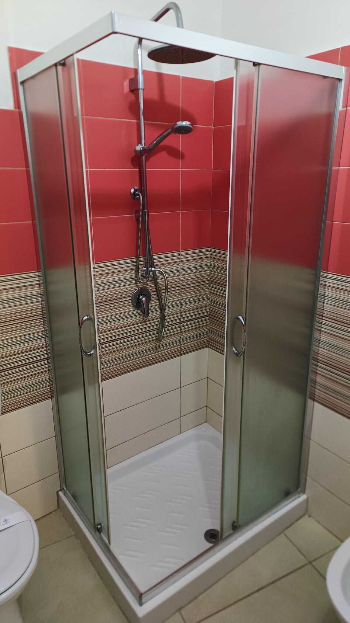 A shower enclosure with a glass door, a handheld showerhead, and a wall-mounted faucet.
