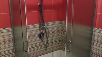 A shower enclosure with a glass door, a handheld showerhead, and a wall-mounted faucet.