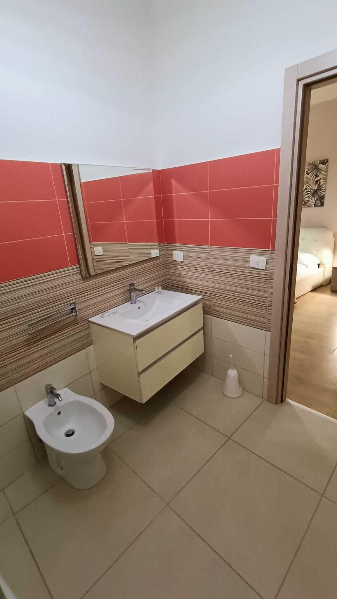 A bathroom with a white sink, a bidet, and red and beige tiled walls.