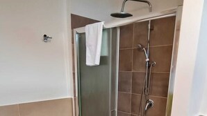 Ett badrum med en dusch som är avskärmad med glasväggar, en tvättmaskin och kaklade väggar.