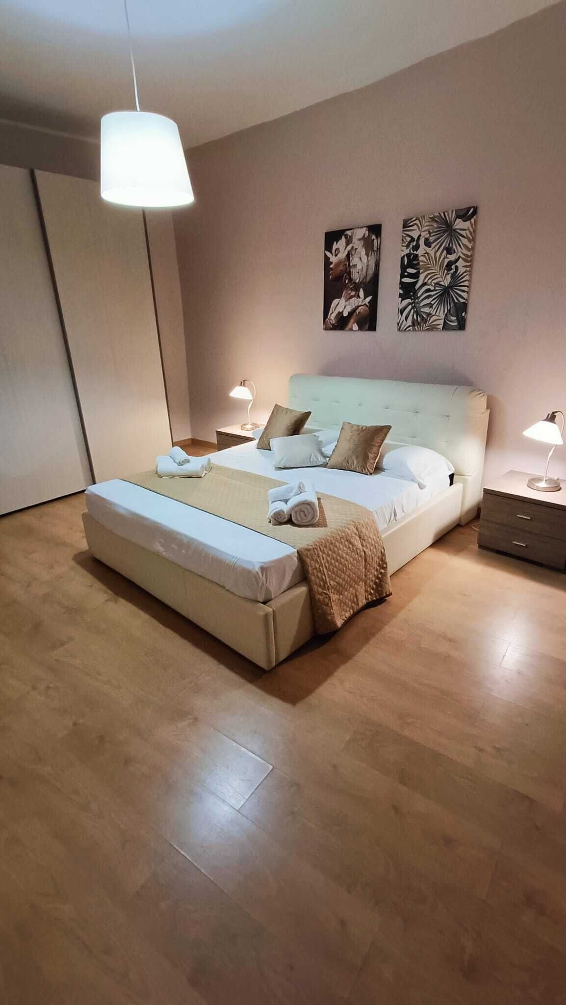 A modern bedroom with a large bed, bedside lamps, and two wall art pieces.