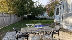 An outdoor patio with a metal table and chairs, a small decorative vase, and a wooden fence in the background.