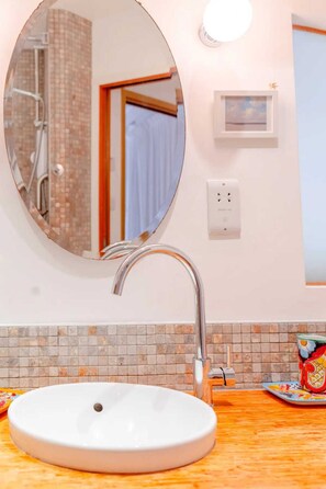 A bathroom with a round mirror, a white sink, and a shower area visible through the mirror.