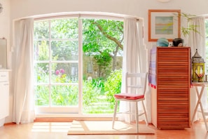 Step into a serene oasis with a curved glass door leading to a lush garden, featuring a comfortable chair, a wooden cabinet, and a small table with a lantern.