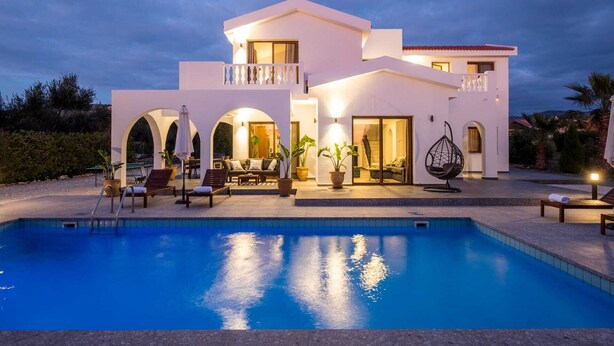 Una casa moderna de dos pisos con piscina, mobiliario exterior y un patio bien iluminado.