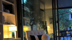 A modern living room with a sofa, a coffee table, and a glass door leading to an outdoor area with a table and chairs. - Maison de Charme (Valence)