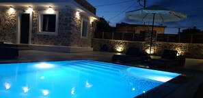 A swimming pool with a stone wall and a patio area with outdoor furniture. - Double Bee Villa with private pool (Oropedio Lasithiou)
