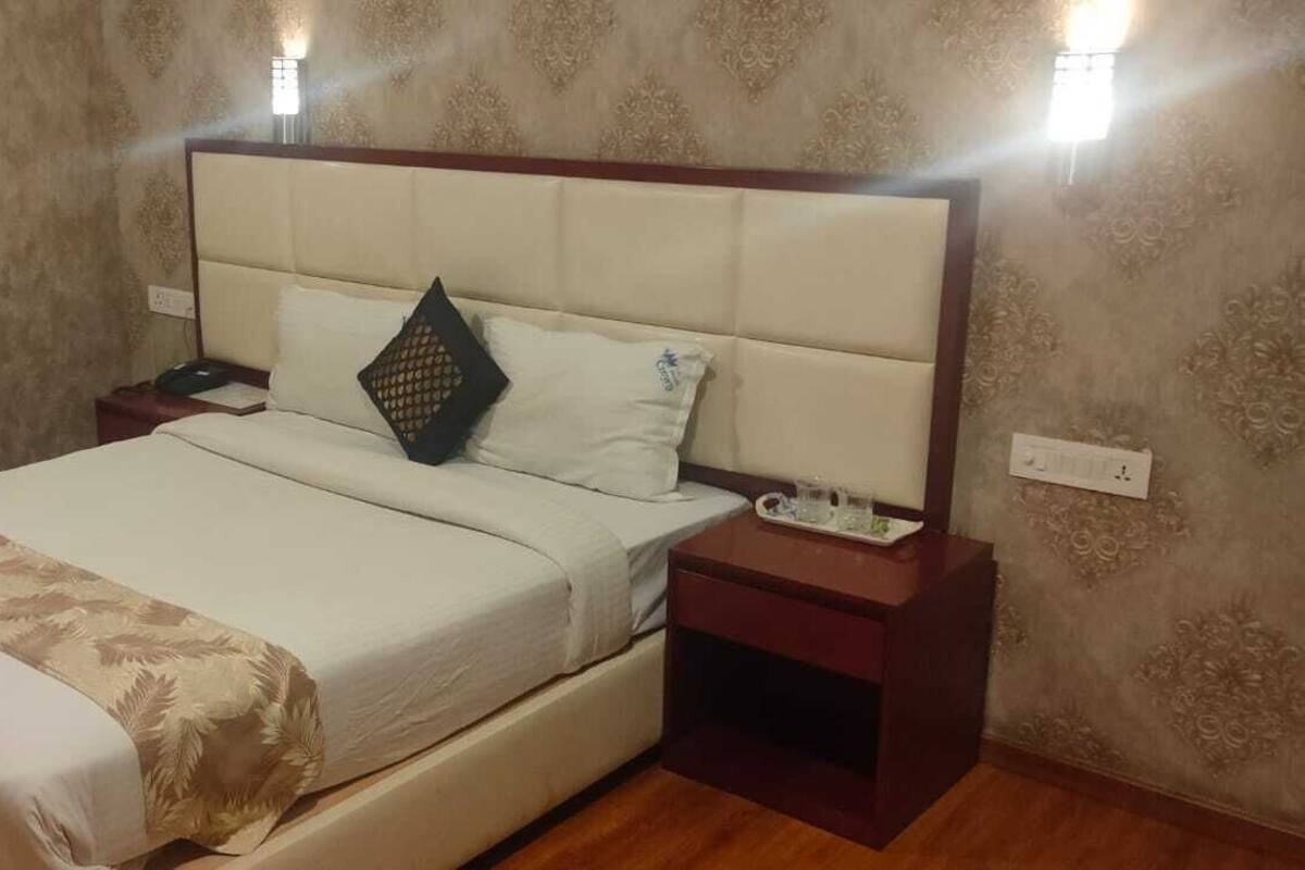 A hotel room with a large bed, a nightstand, a bedside table, and a wall-mounted light fixture.