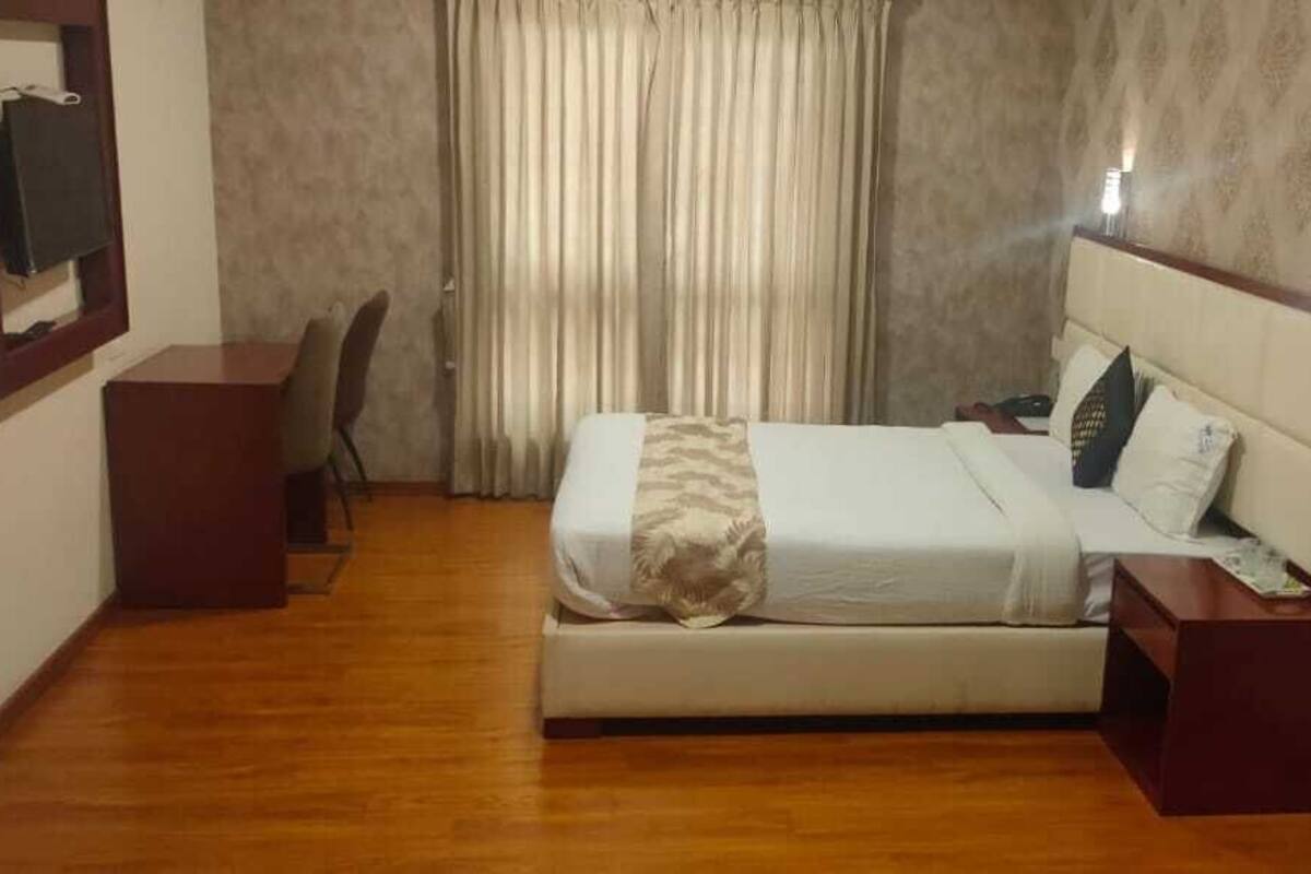 A hotel room with a bed, bedside table, chair, and a TV mounted on the wall.