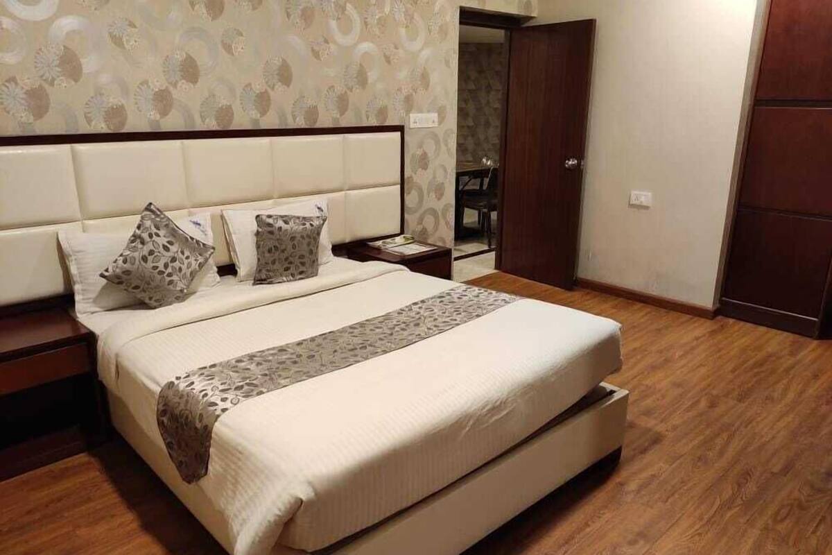 A bedroom with a large bed, two nightstands, a wooden floor, and a patterned wallpaper.
