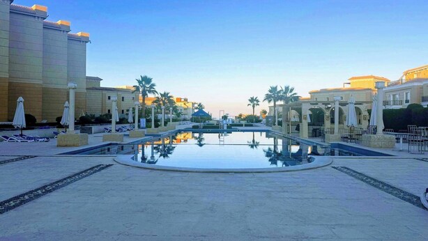 A large outdoor swimming pool with lounge chairs and umbrellas, surrounded by buildings with classical architecture. - 2 Bed Flat - Sleeps 6 - Pool - Parking - Wifi (Hurghada)