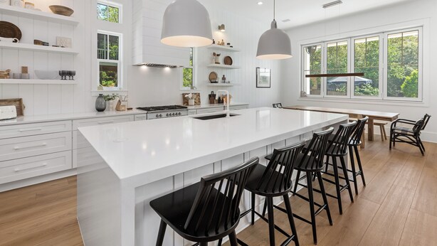 Een ruime keuken met een groot eiland, witte kasten en zwarte barstoelen.