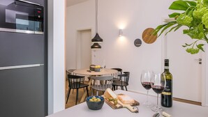 Eine moderne Küche mit Backofen, einem Esstisch mit Stühlen, einer Oliven-Schale, einer Käseplatte, Weingläsern und einer Weinflasche.