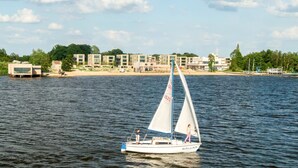 Ein Segelboot auf ruhigem Wasser, im Hintergrund ein Hafen und Gebäude.