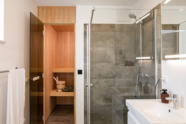 A modern bathroom with a glass-enclosed shower, a wooden sauna, and a white sink.