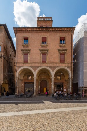 A historic building with a central arched entrance, a sign reading "SALA DA BARBERIA," and outdoor seating for patrons.