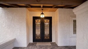 A hallway with a black double door featuring decorative ironwork, a wooden ceiling, and a patterned floor. - Gorgeous and private ranch on expansive 1.2 acres (Scottsdale)