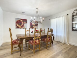 A dining room with a wooden table and chairs, a chandelier, and two floral paintings on the wall.